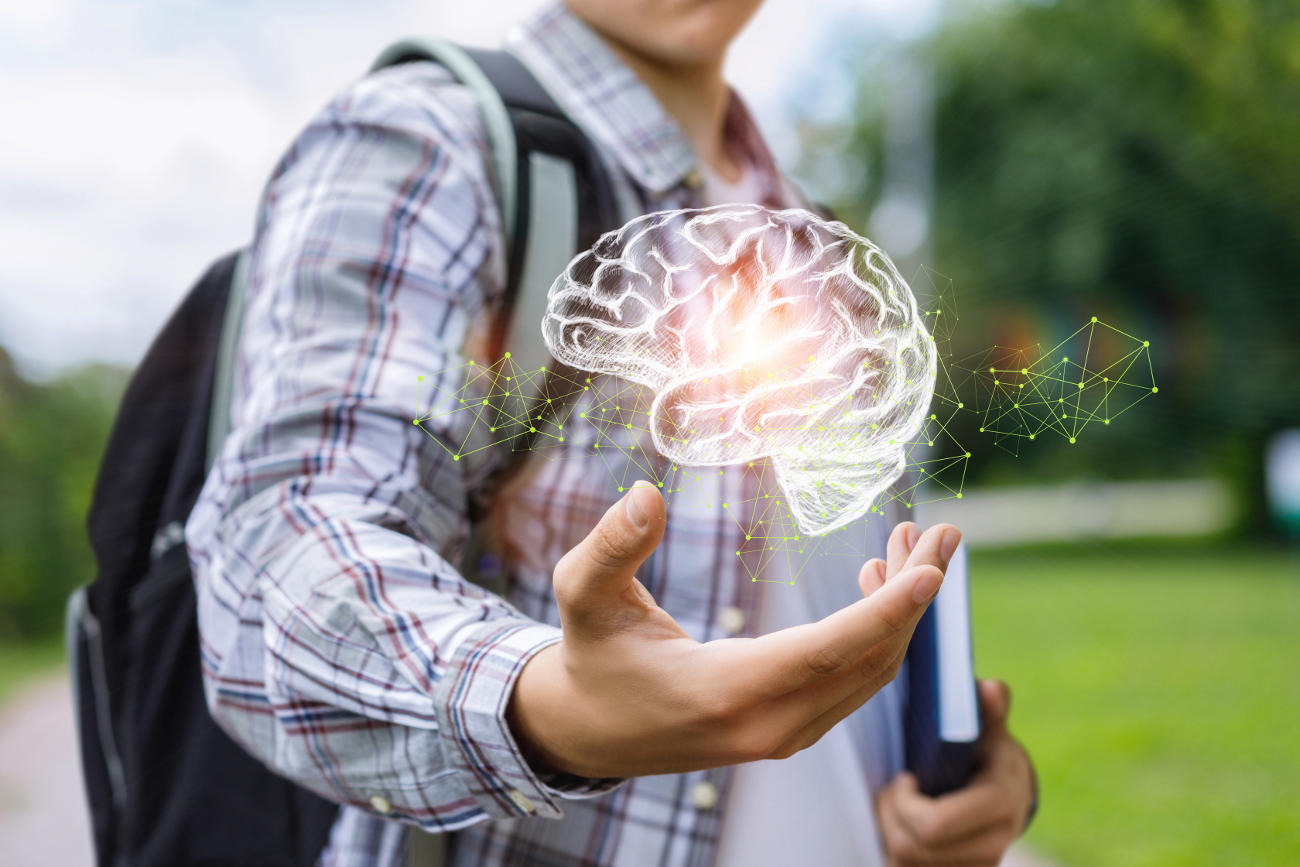 A student's hand is held open with a holographic image of a brain floats above it.